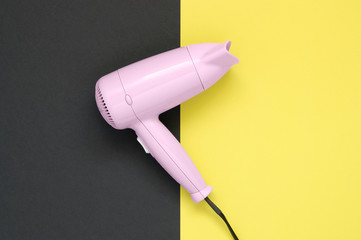 Pink hair dryer on black and yellow background