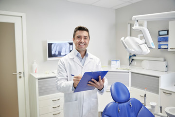 happy male dentist with clipboard at dental clinic