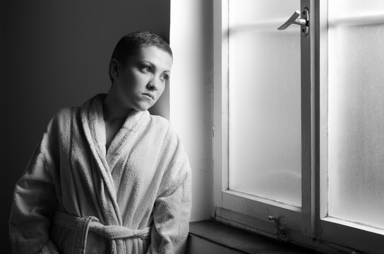 Girl, sad cancer patient looking through hospital window