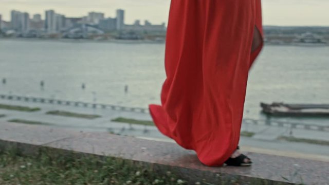 Feet of young woman in a red dress walking in the wind with fluttering dress