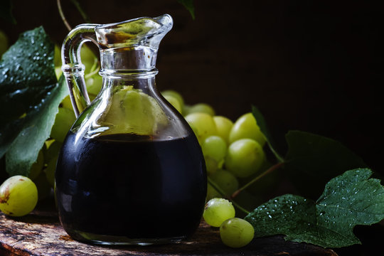Balsamic vinegar in a glass jug, vintage wooden background, rust