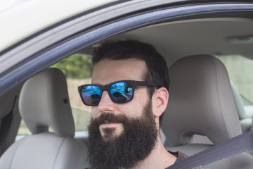 Close up view of young man with beard and sunglasses in the driver's seat of his car with the seat belt fastened.