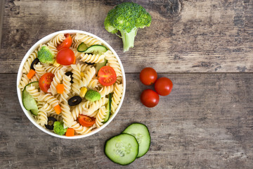 Pasta salad in bowl with vegetables on rustic wooden table
