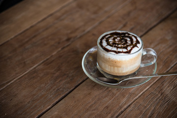 A cup of coffee with pattern in a glass cup on wooden background