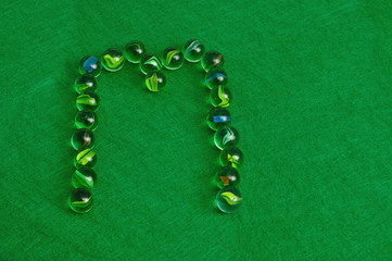 The letter M made out of marbles on a green background
