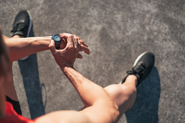 Fitness man resting during outdoor cross training workout reseting watch counter. Fit fitness sport model sitting on a bench outside before running.
