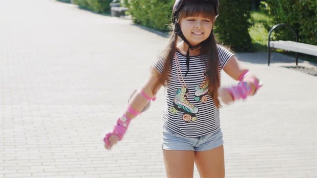 Cute little girl is riding on roller skates / Cute little girl is riding on roller skates summer day on the street. Steadicam shot. Slow Motion.