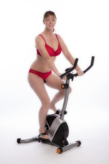 Fototapeta premium WOMAN RIDING AN EXERCISE BIKE - A mid age woman wearing red underwear riding an exercise bicycle