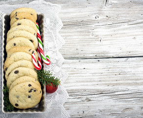 Festive Christmas card. Homemade cookies with chocolate drops for Santa Claus in the baking dish is decorated  fir branches, red balls, cones, candy striped staffs. selective focus