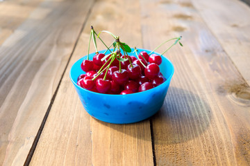 Ripe cherries in the blue bowl on wood background.
