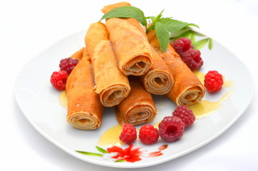 Блины с начинкой сложенны трубочкой на тарелке политы медом листья мяты и свежие ягоды малины рядом