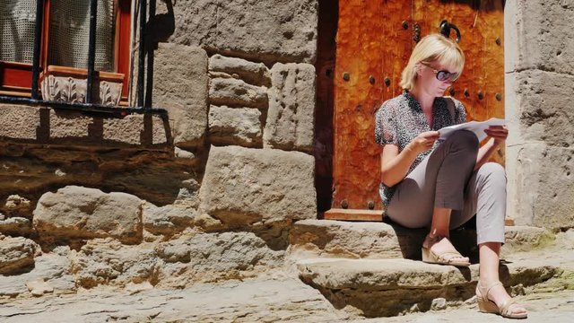 Female tourist sitting on the stairs of an old house in the village of Rupit. Read the guide