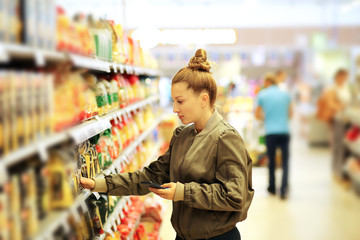 Woman shopping in supermarket reading product information. Checking list.
