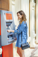 Happy brunette woman withdrawing money from credit card at ATM