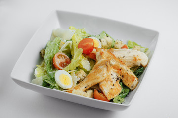Caesar salad with cheese, eggs, herbs, chicken, and tomatoes in the white plate