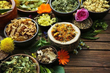 Herb selection and fresh flowers in bowls on wooden background