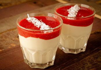 Creamy dessert with strawberry sauce and coconut flakes in glasses
