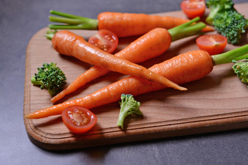 Fresh baby carrots and cherry tomatoes on wooden cutting board closeup