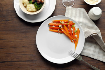 Plate of slices baby carrots with herbs on wooden table, top view