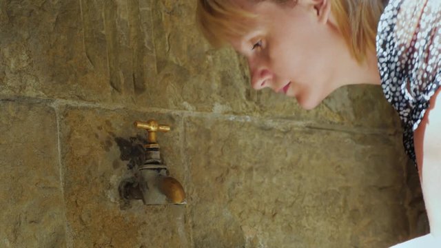 Tired from the heat Woman washes with ancient crane in a stone wall. Town of Rupit Catalonia