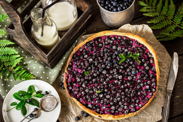 Homemade pie with bilberry and milk on dark wooden table