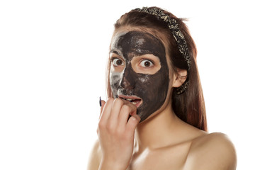 surprised young woman with mud mask on her face