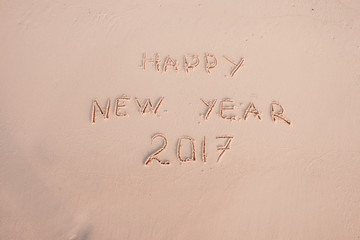 Fototapeta na wymiar 2016 2017 inscription written in the wet yellow beach sand being washed with sea water wave. Concept of celebrating the New Year at some exotic place