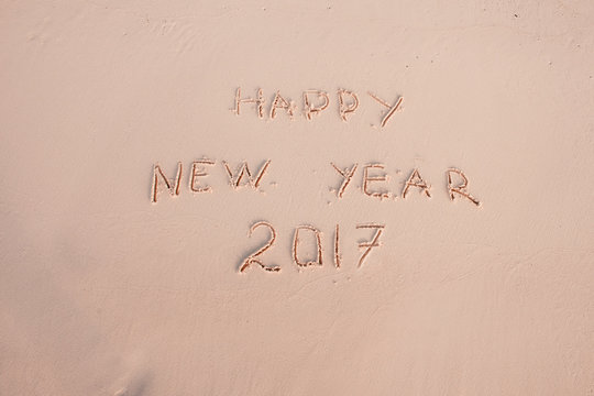 2016 2017 inscription written in the wet yellow beach sand being washed with sea water wave. Concept of celebrating the New Year at some exotic place