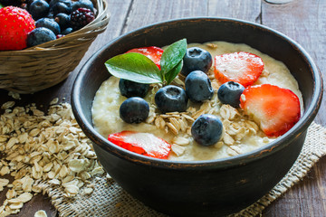 Oatmeal porridge in brown pottery bowl with ripe berries