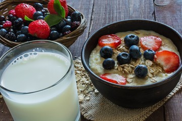 homemade oatmeal porridge with berries and glass of milk on wooden table