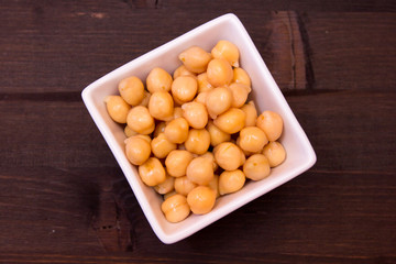 Boiled chickpeas on a square bowl on a wooden table seen from above