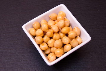 Boiled chickpeas on a square bowl on a slate top seen from above