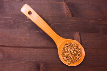 wooden spoon with coriander seeds on a wooden table seen from above