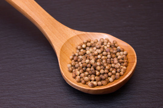 wooden spoon with coriander seeds on a slate floor