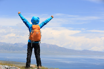 cheering successful woman backpacker open arms on mountain peak