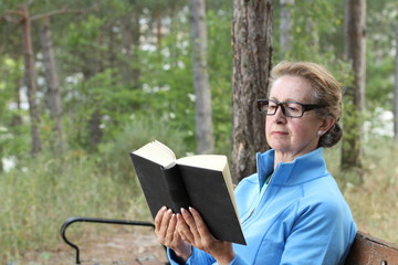 Senior Woman Relaxing On Park Bench Reading a Book