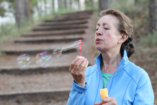 Senior woman blowing soap bubbles in summer park.