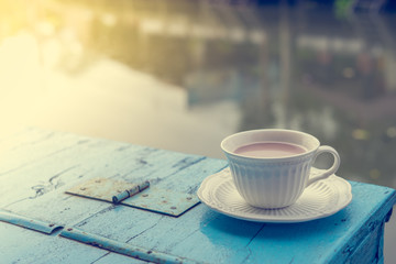 Cup of hot coffee on old wooden table and view of sunrise in the river background.Vintage tone with copy space.