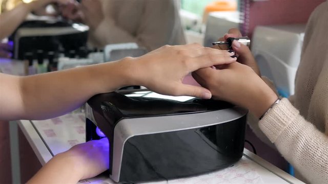 woman in a nail salon receiving a manicure by a beautician with nail file. Woman getting nail manicure. Beautician file nails to a customer. Blurred background
