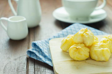 Close-up eclairs with custard cream and cup of coffee on wooden dish on old wooden wood table background texture 
