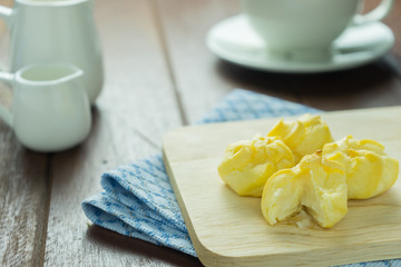 Close-up eclairs with custard cream and cup of coffee on wooden dish on old wooden wood table background texture 