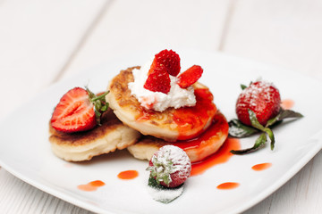 Pancake dessert with strawberries, cream and topping on white wooden table. Appetizing serving of sweet at restaurant