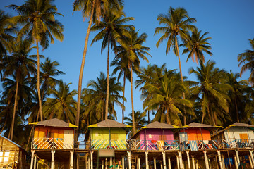 Colorful huts on the sandy beach with palm trees background in G - obrazy, fototapety, plakaty
