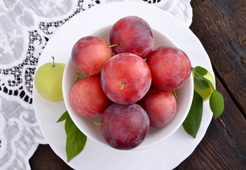 Red plums in the white bowl on wooden table