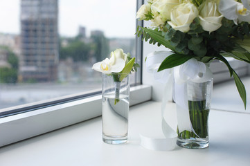 Beautiful wedding bouquet in a glass vase. Flowers on white windowsill. Boutonniere in a small vase. The window in the background.