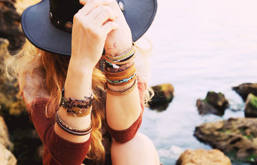 Female hands with boho chic bracelets holding black hat - obrazy, fototapety, plakaty