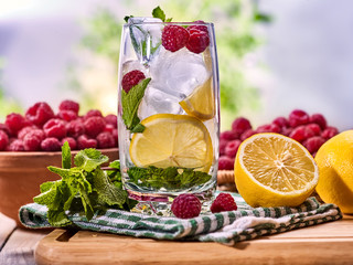 On wooden boards glass with raspberry alcohol cocktail and ice cubes. Cocktail number two hundred cocktail raspberry mojito with raspberry bowl and napkin. Country life. Outdoor. Light background.