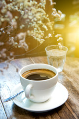 White coffee cup with dry flower on wooden table.