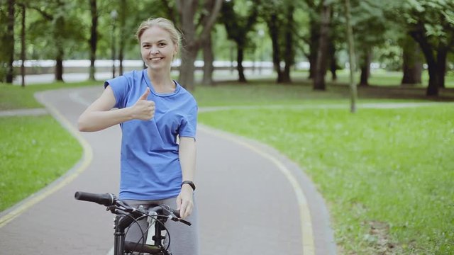 Portrait of pretty young woman with bicycle in a park smiling with thumbs up gesture