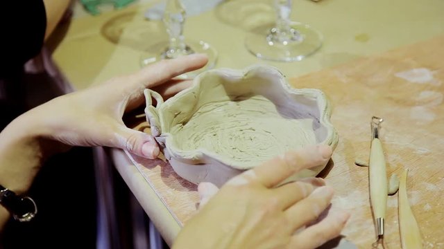 Young woman sculpts pot from white clay in workshop with enthusiasm